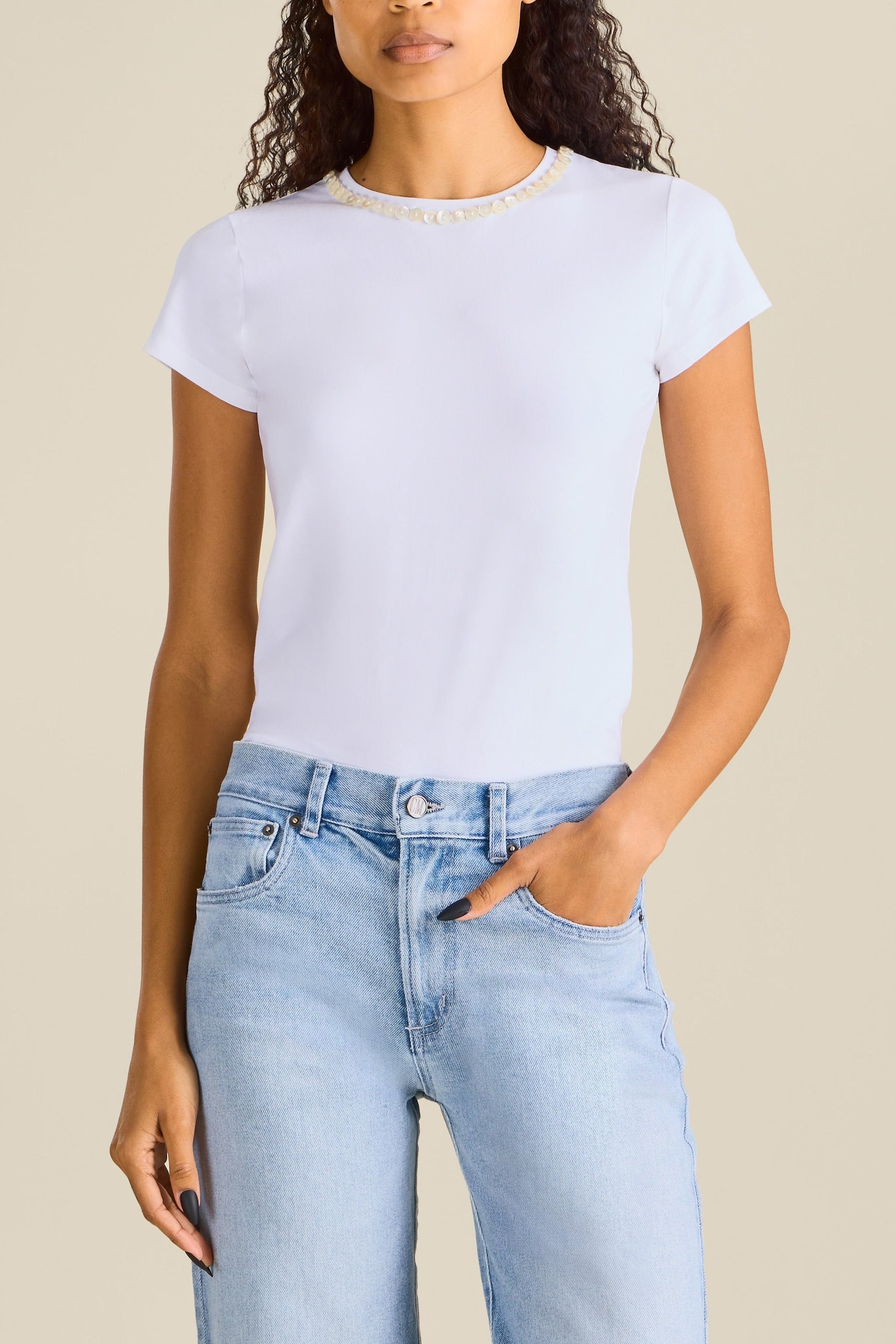 Woman wearing light blue jeans with rips and a white t-shirt on a beige background