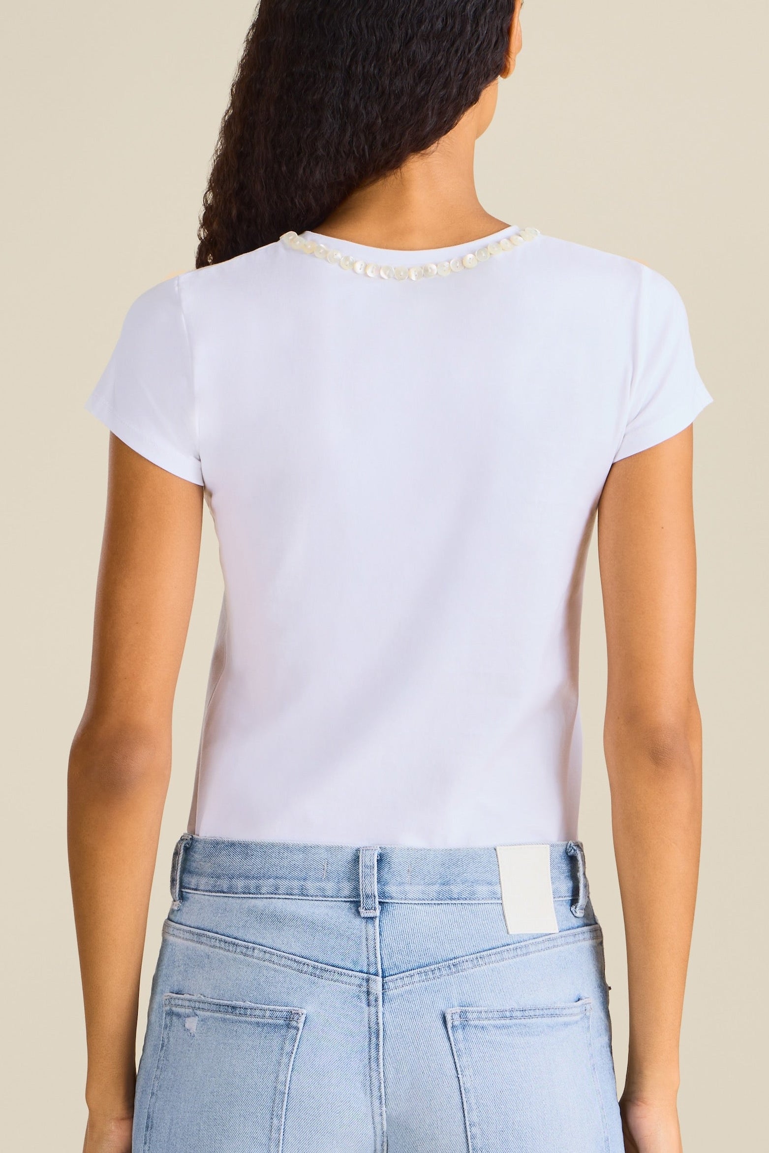 Woman wearing light blue jeans and a white t-shirt on a beige background