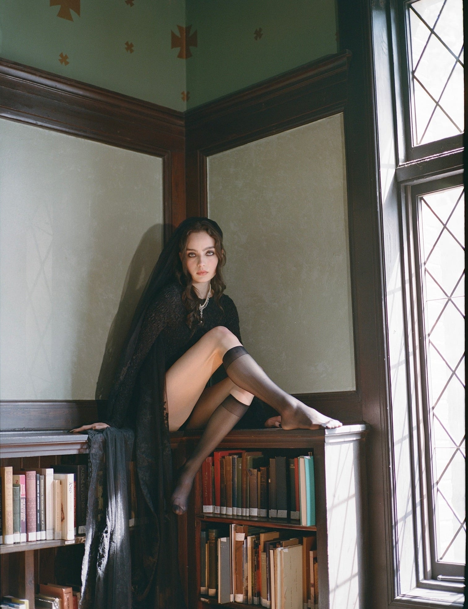 Woman sitting on a bookshelf in a room with a large window