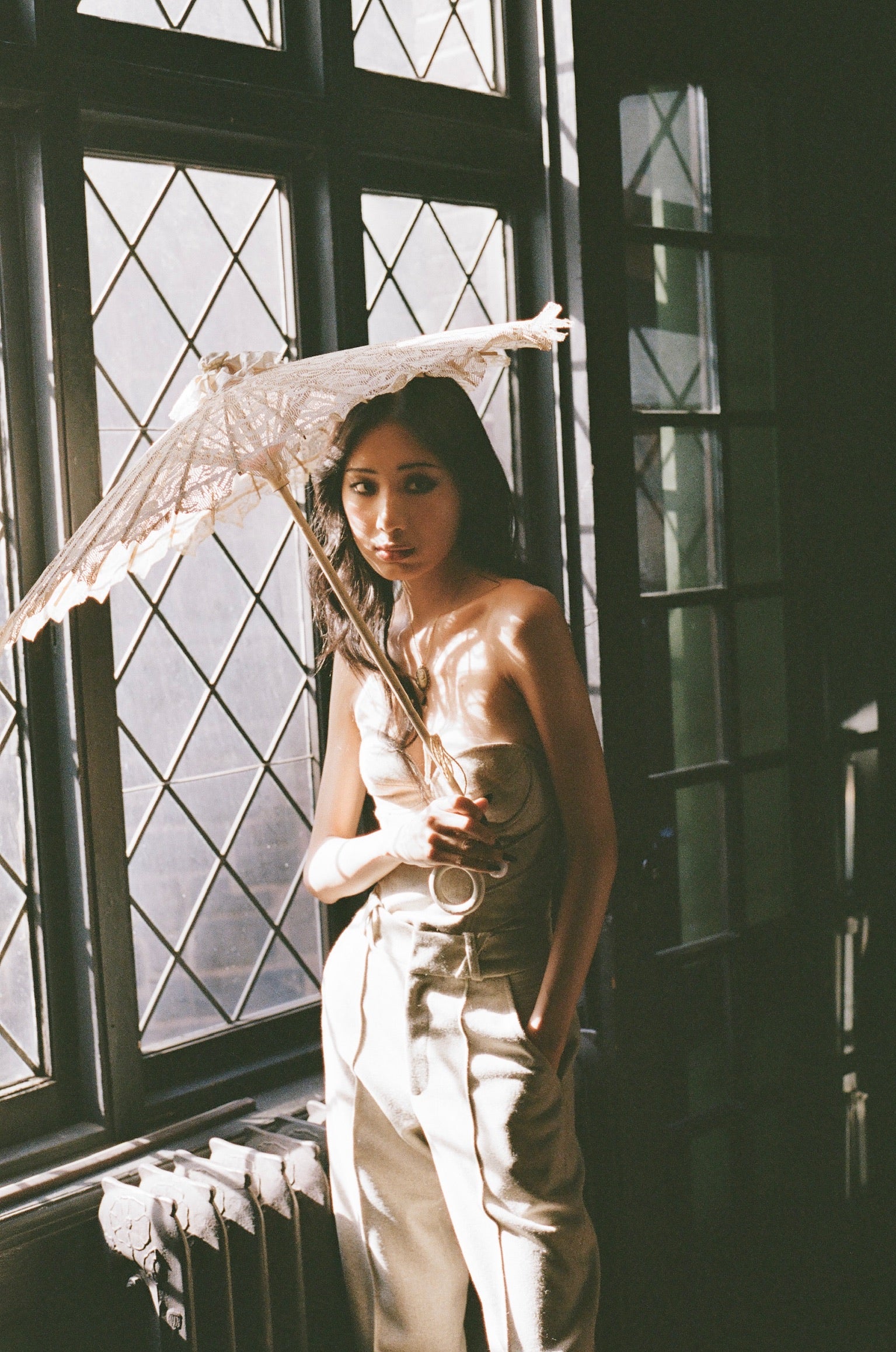 Woman holding a lace parasol in front of large windows